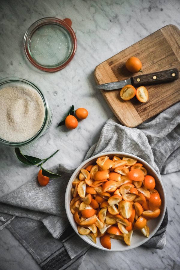 a bowl of sliced and seeded kumquats and a bowl of sugar on a counter