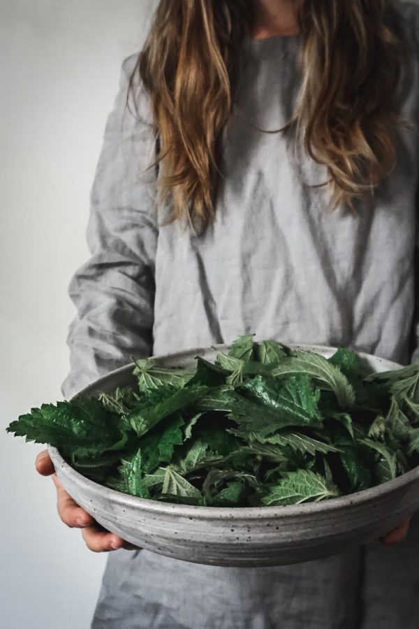 Woman in grey dress holds a bowl of stinging nettles