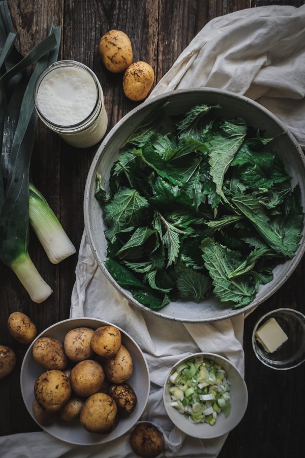 Ingredients for nettle soup: potatoes, leeks, and stinging nettles laid out on table. 