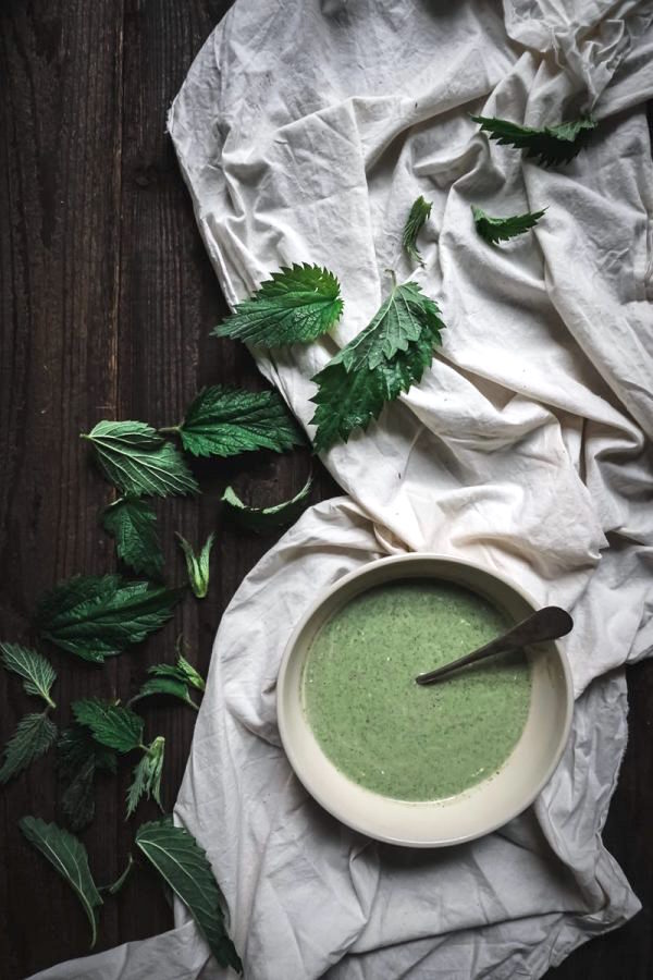 bowl of green nettle soup on table decorated with cloth and loose nettle leaves