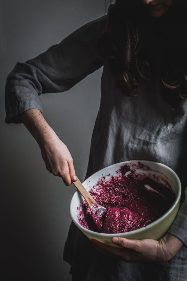 closeup of arm stirring red cake batter in a yellow bowl to show the bright red color of this red velvet cake batter made without food coloring.