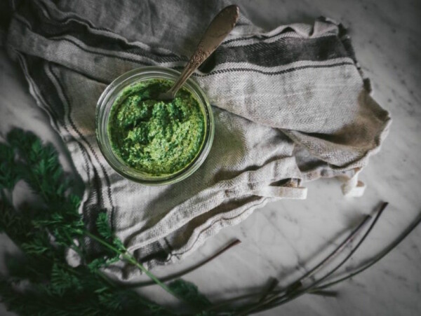 jar of carrot top pesto sitting on a kitchen towel on marble counter