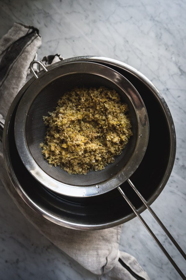 Strainer filled with elderflowers rests on a bowl. 