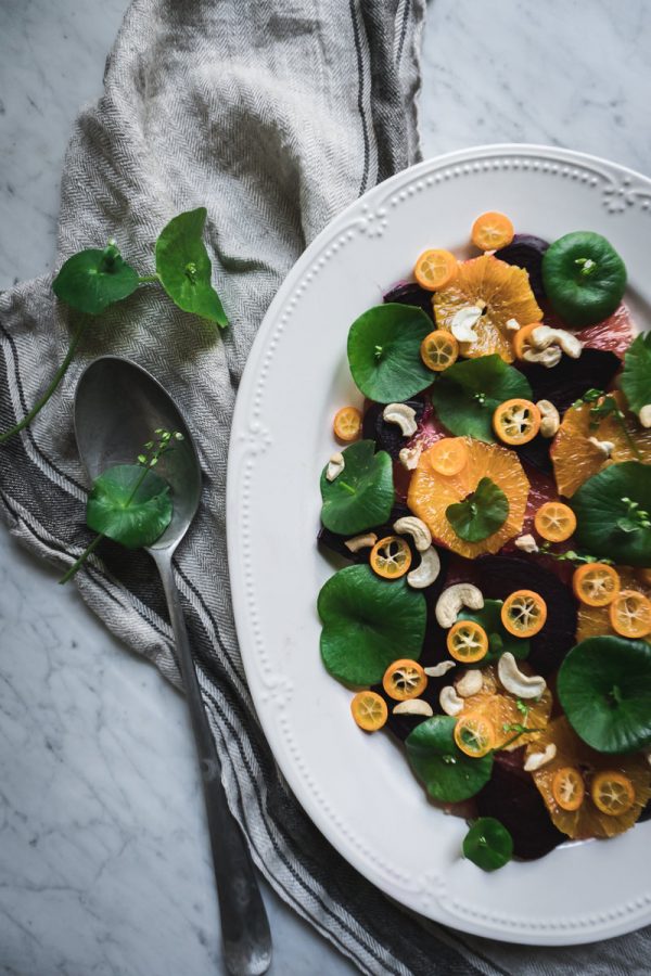 Bowl of miner's lettuce, beets and citrus salad on a marble counter.