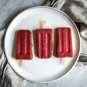 three strawberry popsicles on a white plate on a marble counter