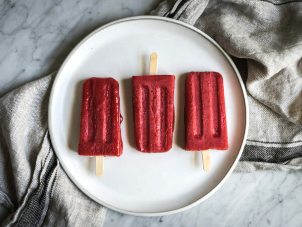 three strawberry popsicles on a white plate on a marble counter