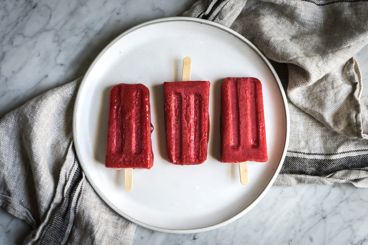 three strawberry popsicles on a white plate on a marble counter