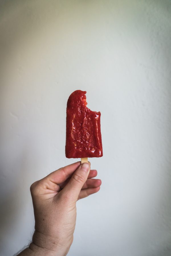 hand holding a strawberry popsicle with a bit taken out