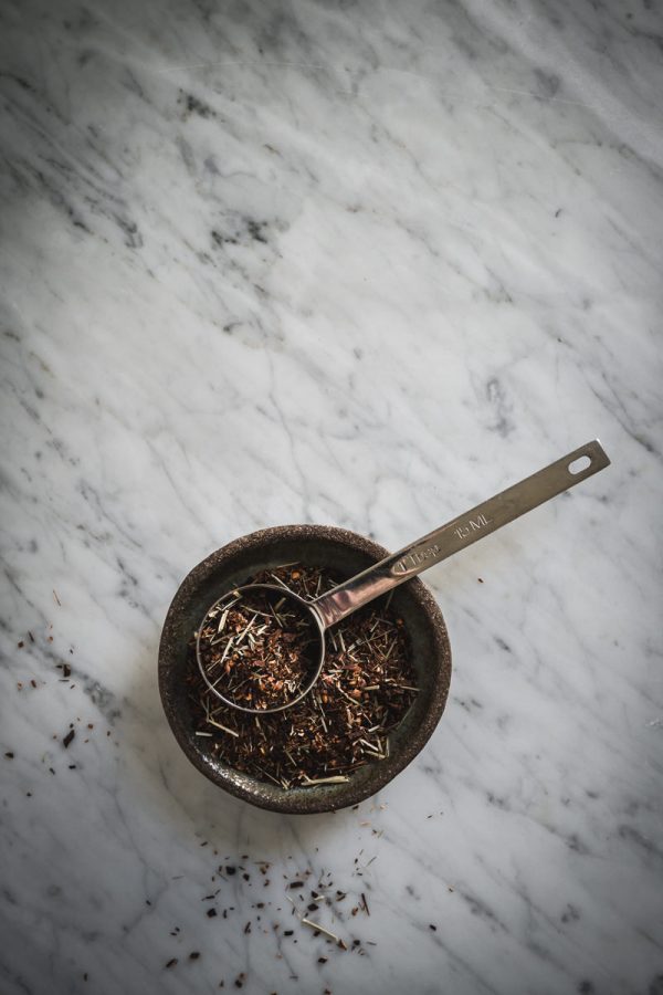 a tablespoon measuring spoon rests in a ceramic bowl of loose leaf tea for making sun tea