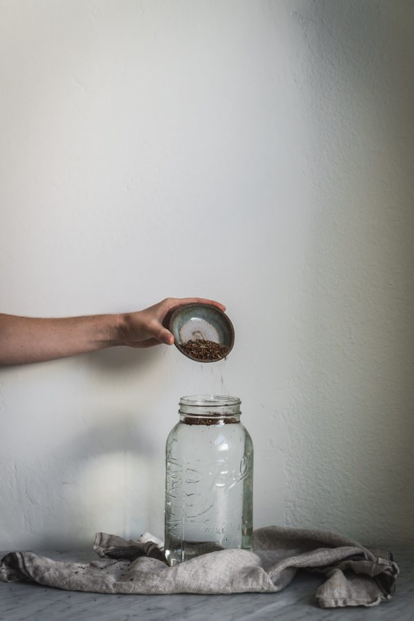 hand pouring tea leaves into jar of water