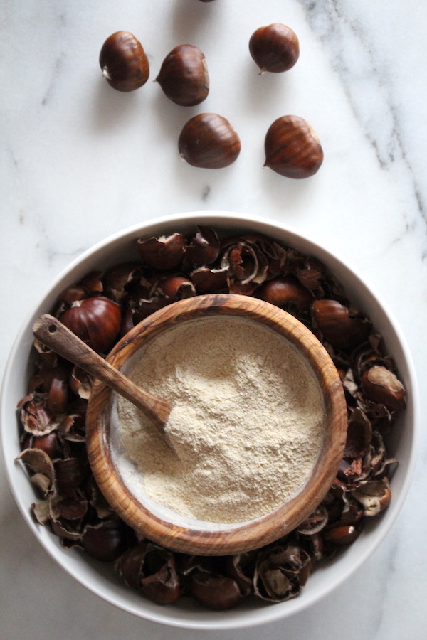 Homemade chestnut flour in a bowl amongst fresh chestnuts and chestnut shells.