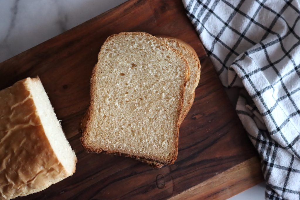 Sliced loaf of bread machine honey white bread on a wooden board showing soft crumb