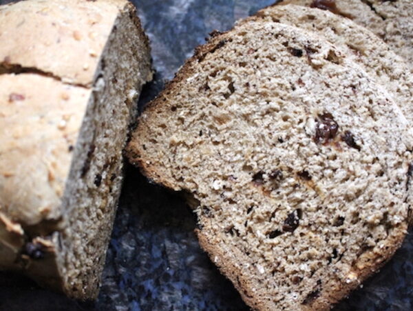 Sliced loaf of bread machine cinnamon raisin bread on a cutting board showing plump raisins in a tender crumb