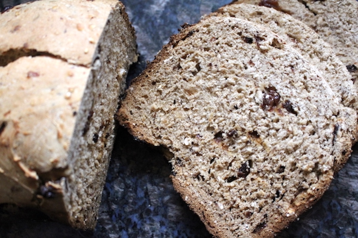 Sliced loaf of bread machine cinnamon raisin bread on a cutting board showing plump raisins in a tender crumb