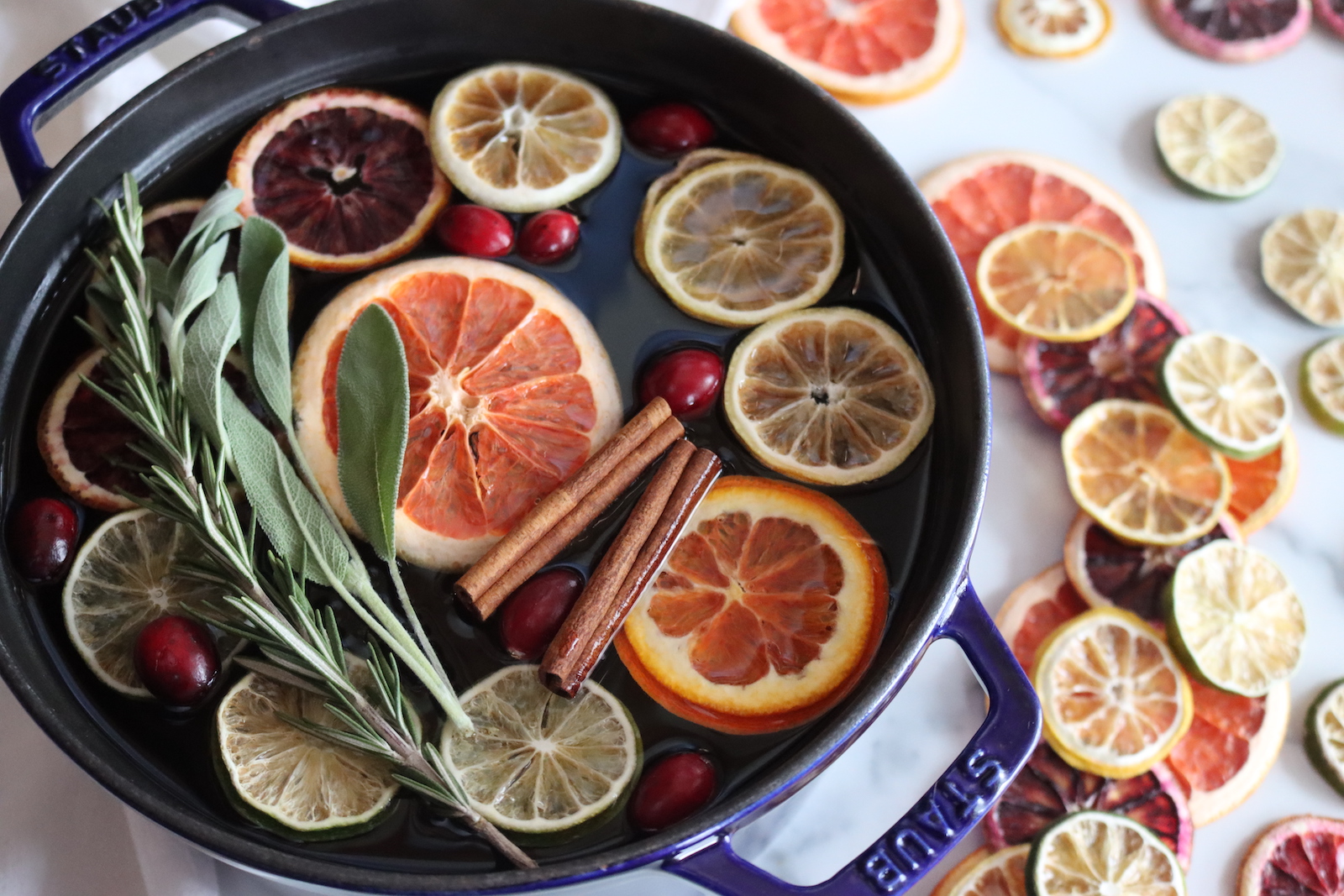 Close-up of a simmer pot with floating dried orange, grapefruit, lemon, and lime slices, cranberries, rosemary, and sage